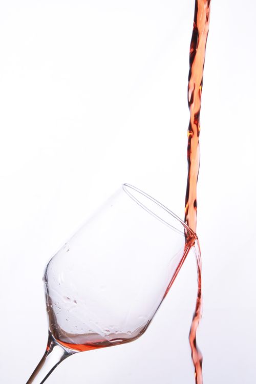 Free Artistic capture of rosé wine pouring into an angled wine glass against a white background. Stock Photo