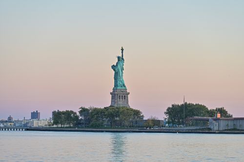 Free A beautiful sunset view of the Statue of Liberty and the New York City skyline. Stock Photo