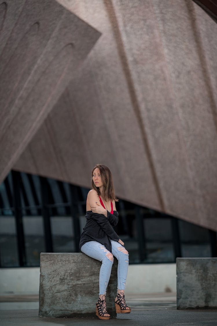 Woman Sitting On Cube Near Modern Building