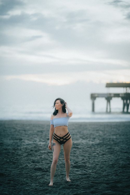 Woman in Bikini Sitting on Beach Sand Near a Jetty · Free Stock Photo