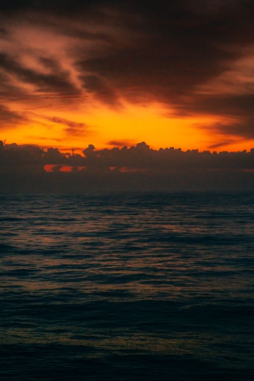 Free Stunning ocean view at sunset with dark clouds and vibrant orange sky, creating a dramatic seascape. Stock Photo