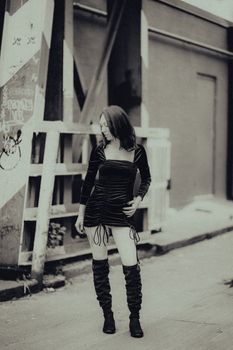 Stylish woman in a black dress and boots posing on an urban street in monochrome.