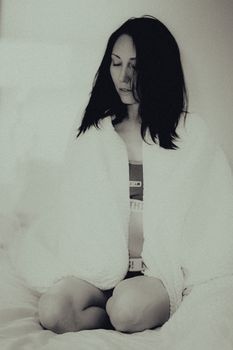 A serene black and white portrait of a woman sitting indoors, enveloped in a cozy blanket.