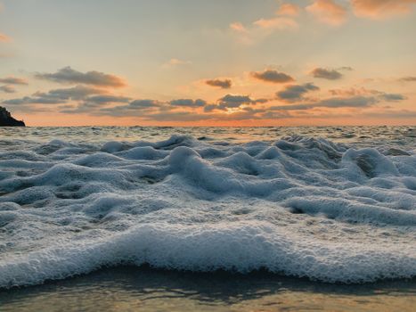 Captivating view of foamy ocean waves under a glowing sunset, creating a serene seaside atmosphere.