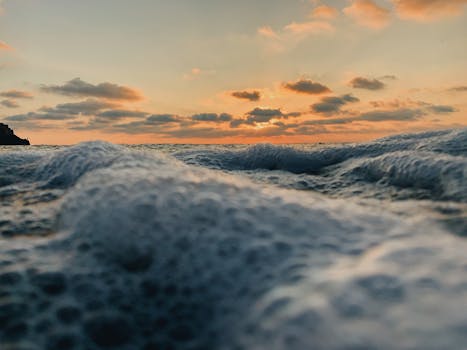 A dramatic ocean sunset with crashing waves and foamy sea surface creating a serene seascape.