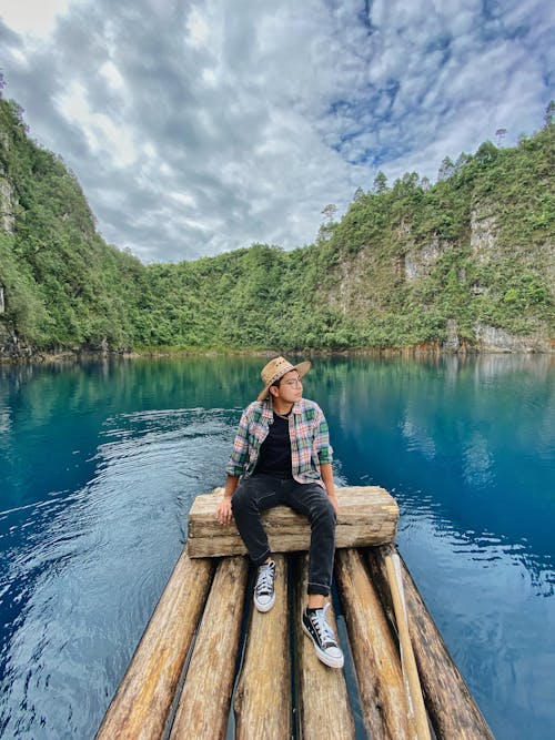 Man Sitting on Wooden Logs on a Body of Water