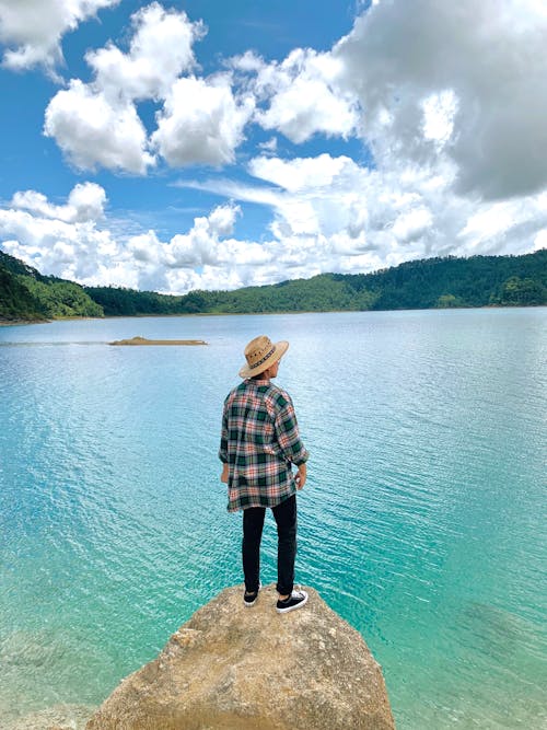 Person in Plaid Dress Shirt Standing on Rock Near Body of Water 