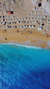 Stunning aerial view of a sandy beach with sun loungers, umbrellas, and turquoise waves.