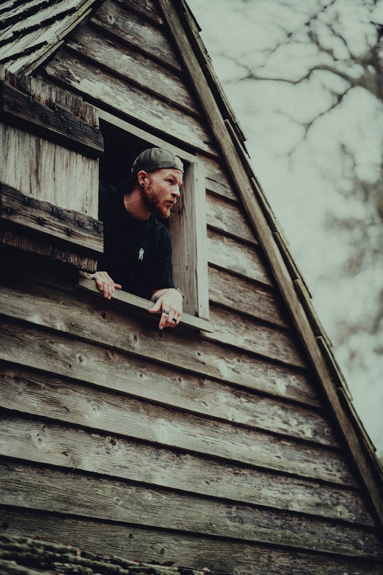 Man Looking Out Of Window Of Wooden Cabin