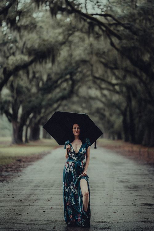 Free A serene moment captured as an elegant woman walks under an umbrella along a lush forest pathway. Stock Photo