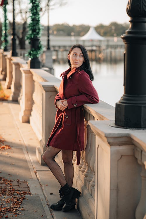 Woman in Red Coat Leaning on Concrete Railing