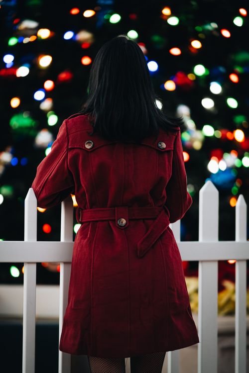 Free Back view of a woman in a red coat enjoying colorful holiday lights at night. Stock Photo