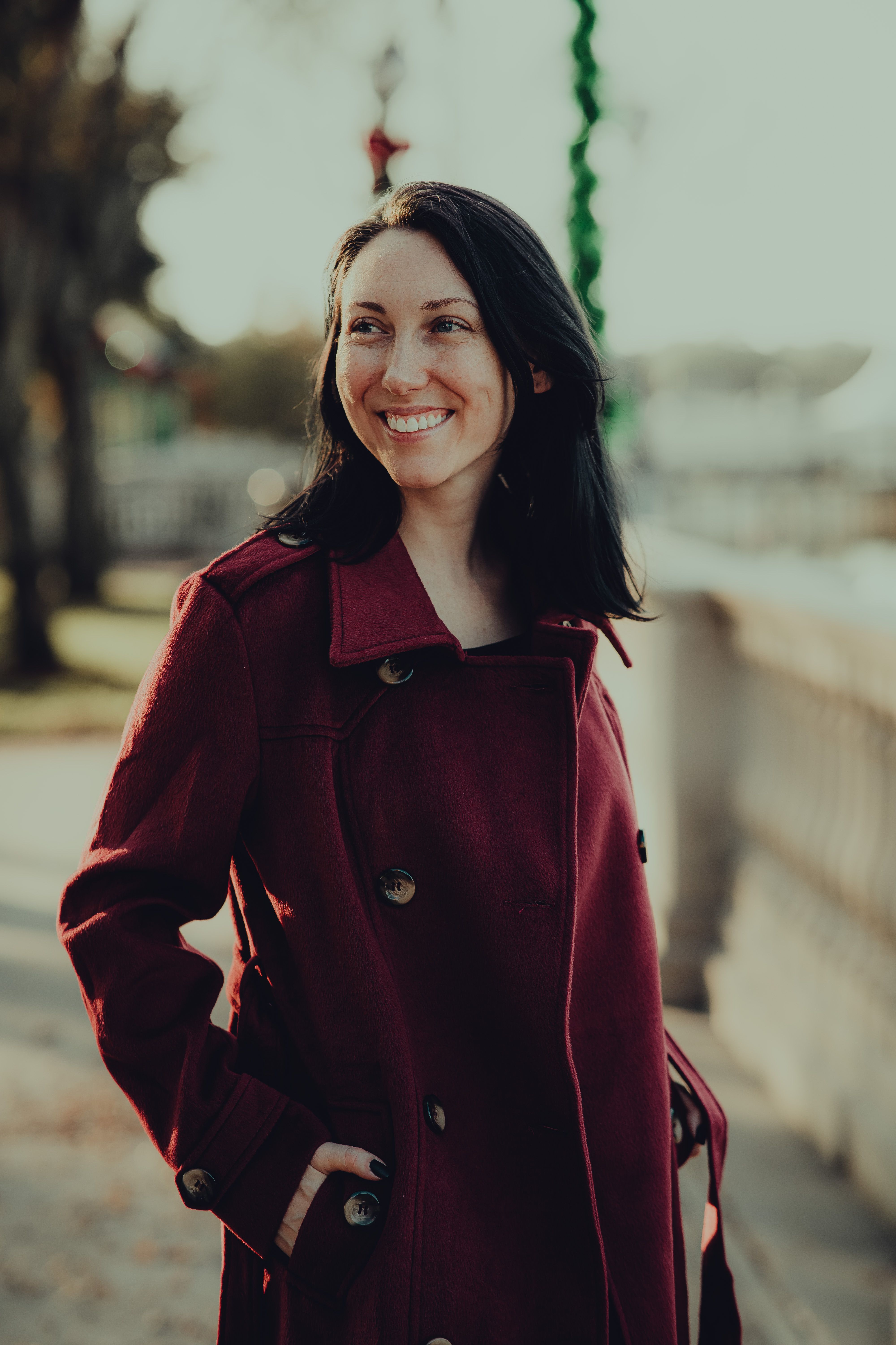 Smiling woman in a burgundy coat enjoying a sunny day outdoors, exuding warmth and elegance.