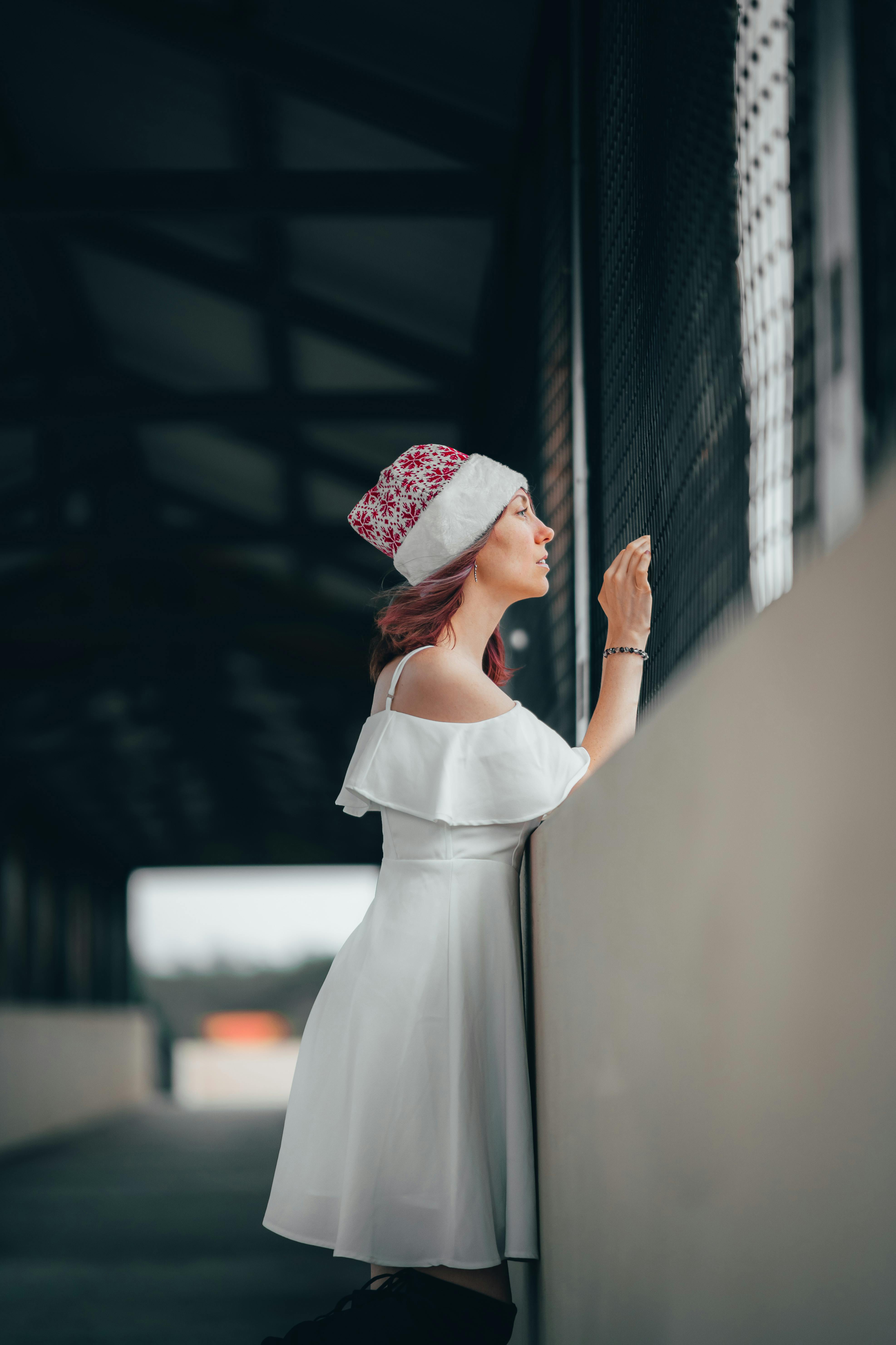 Free Profile view of a woman wearing a white dress and Santa hat, standing on a covered bridge. Stock Photo