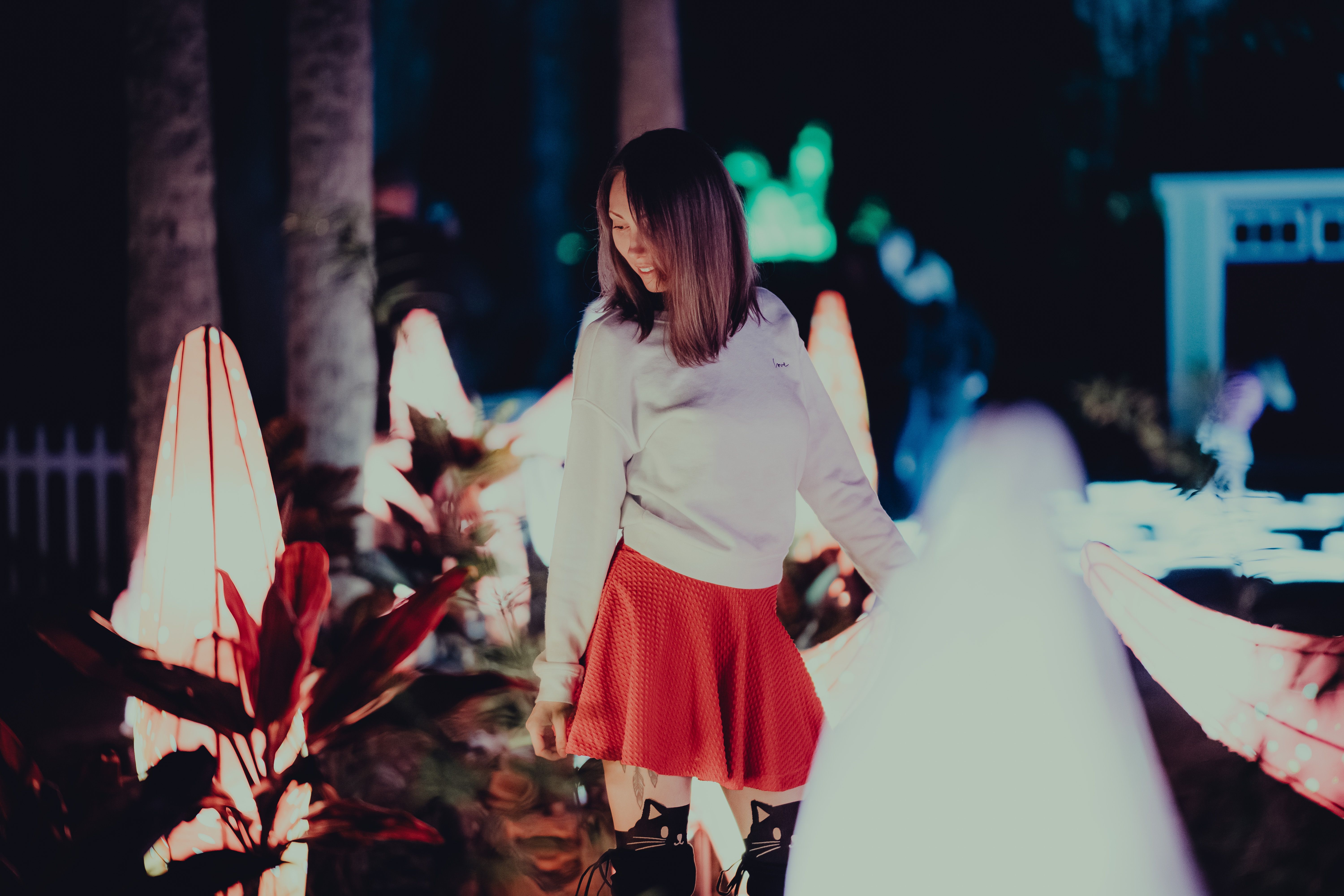A woman in a red skirt stands amidst illuminated sculptures at night, creating a dreamy atmosphere.