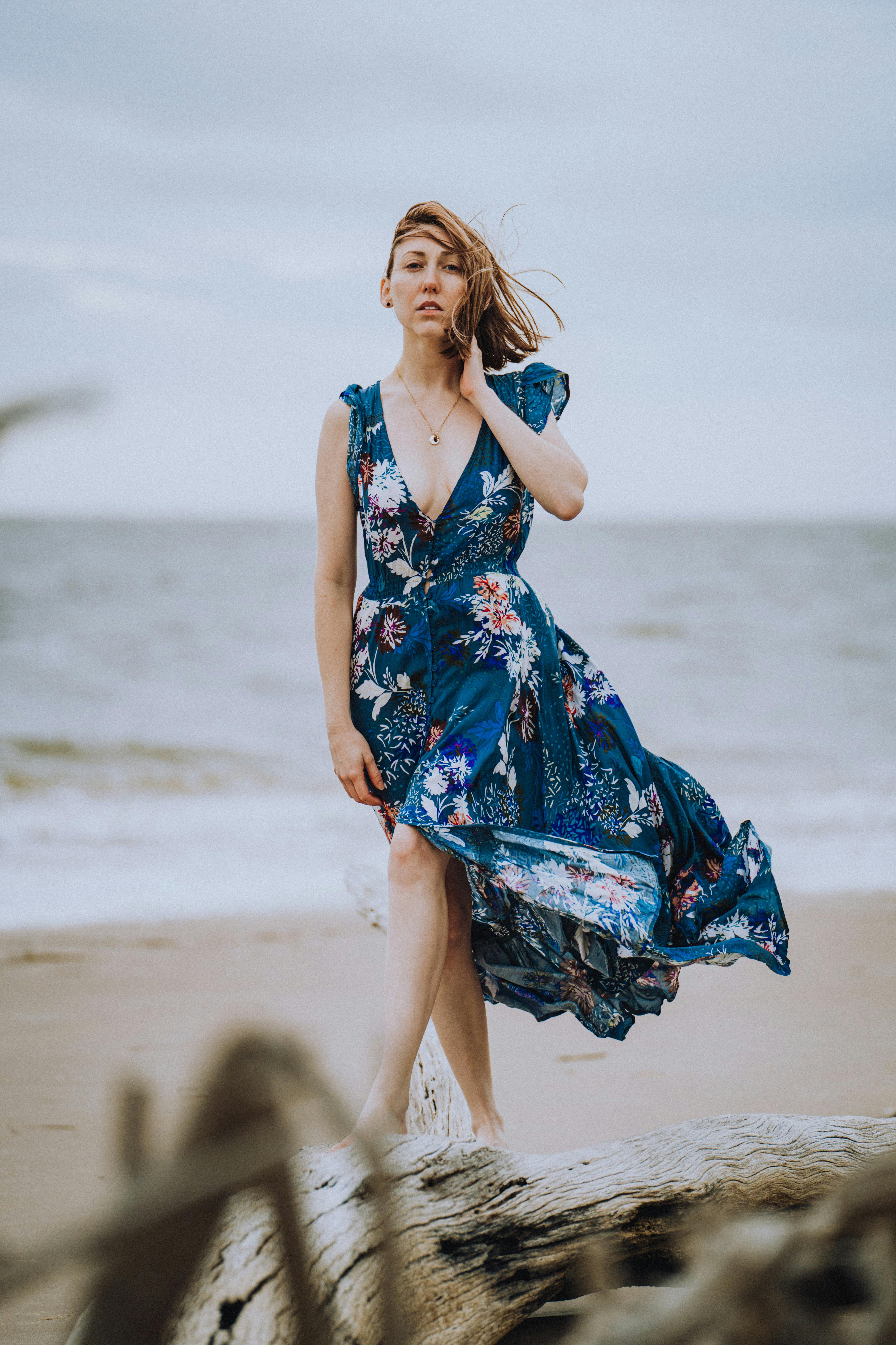 一位身穿花卉连衣裙的女子在微风轻拂的海滩上摆姿势，背景是大海