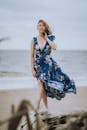 一位身穿花卉连衣裙的女子在微风轻拂的海滩上摆姿势，背景是大海