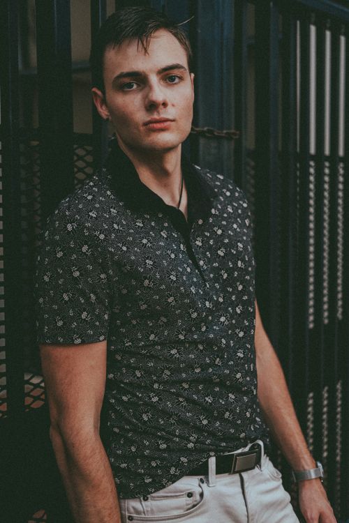Free Stylish young man in a floral polo shirt posing confidently indoors. Stock Photo