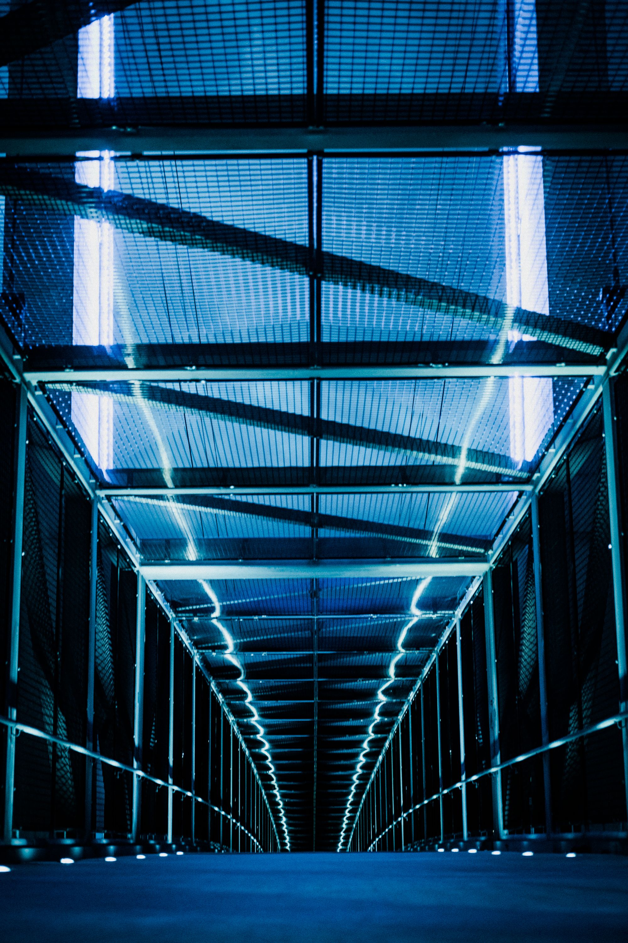A long corridor of server racks under blue light, seen from a low angle