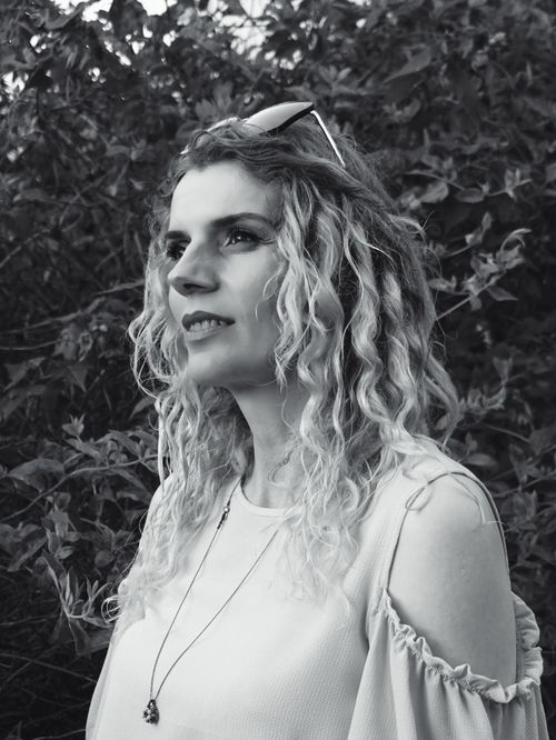 Free Black and white portrait of a woman with curly hair and sunglasses, set against a leafy background. Stock Photo