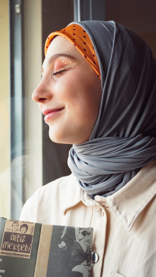 Woman in a Headscarf Holding a Book and Smiling 