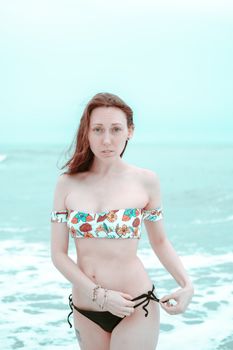 Portrait of a woman in floral swimsuit on a beach, showcasing summer fashion.