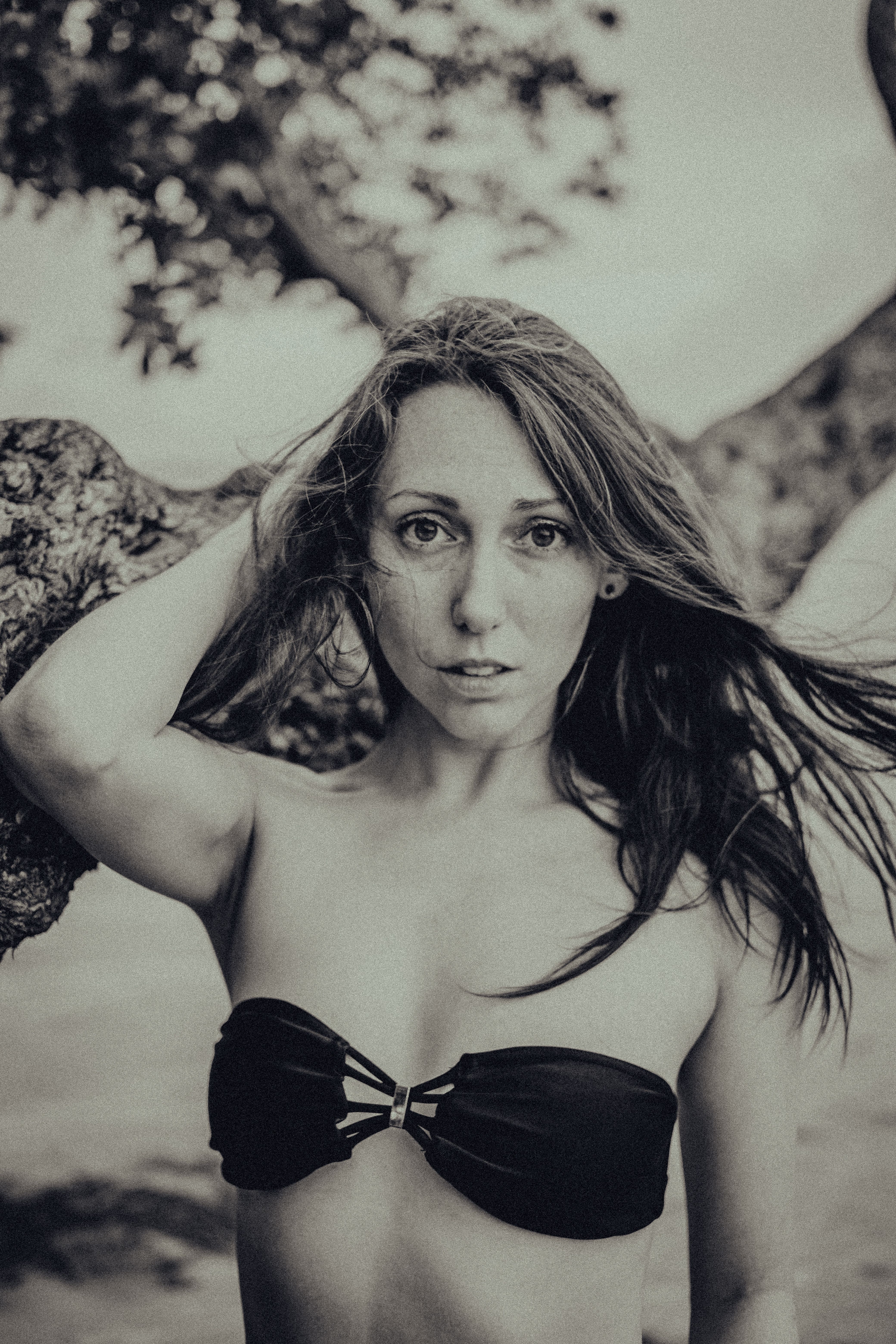 Grayscale portrait of a woman with long hair in a black bikini top outdoors.