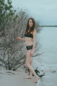 Woman in a black bikini walking by the shoreline on a peaceful beach during summer.