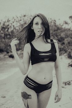 Stylish black and white photo of a woman in black swimwear posing on a sandy beach.