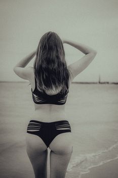 A woman in a stylish black bikini posing at the beach in a black-and-white shot.
