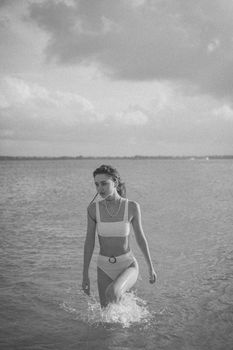 Graceful monochrome shot of a woman walking through water in elegant swimwear.