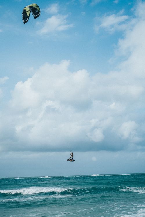 Free A kite surfer performing an aerial stunt over the ocean under a vibrant blue sky. Stock Photo