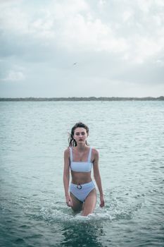 A woman in a white bikini walks confidently from the sea, embodying summer relaxation.