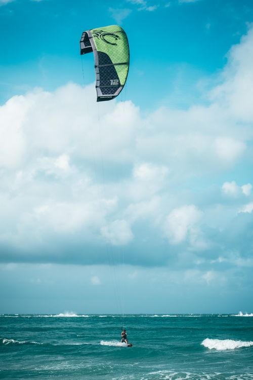 Free A man enjoying kitesurfing on turquoise ocean waves under a bright blue sky. Stock Photo