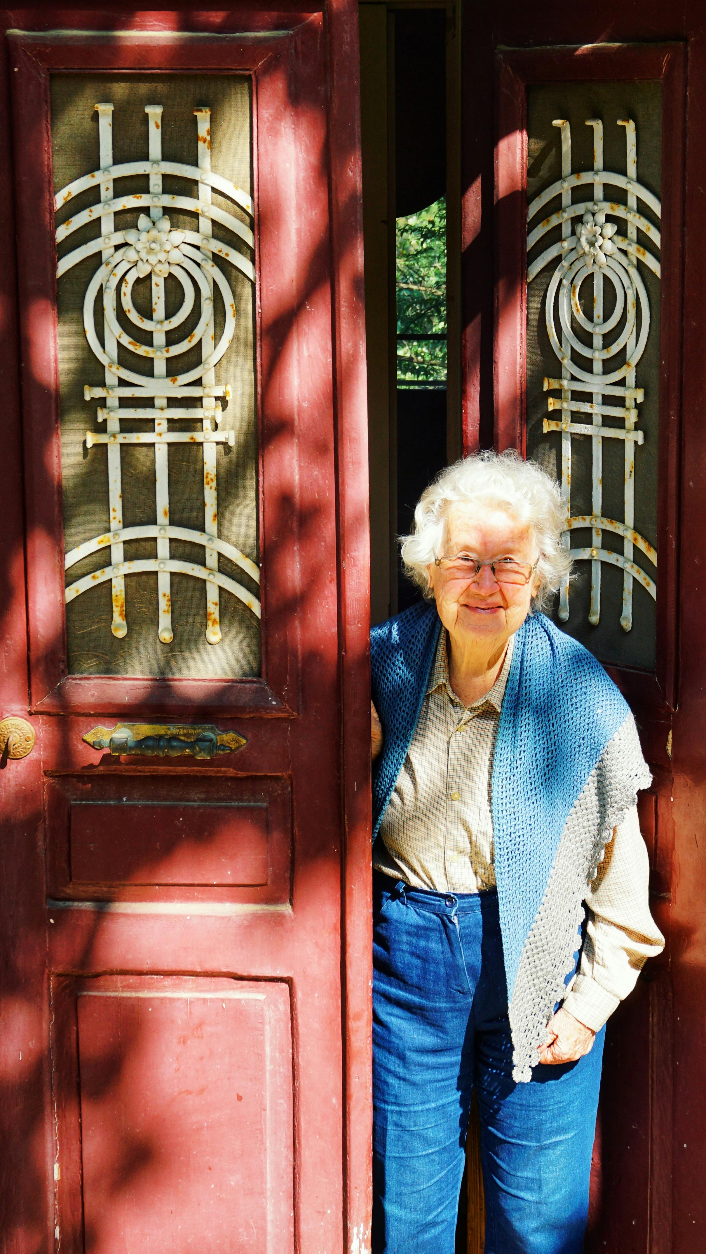 Elderly woman with gray hair smiling in a doorway, wearing denim.