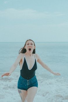 A joyful young woman runs through ocean waves on a sunny day, embracing summer fun.