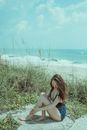 Woman in Blue Bikini Sitting on Green Grass Field Near Body of Water
