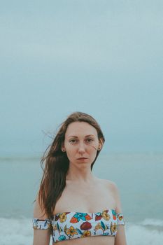 Portrait of a woman in a floral swimsuit standing by the sea with a serene expression.