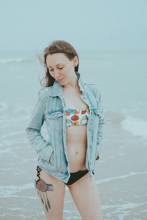 Free Woman in Bikini and Denim Jacket Standing on Beach Stock Photo