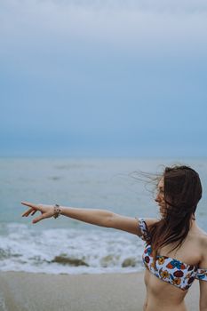 Side view of young woman in floral bikini pointing towards the sea on a summer beach.
