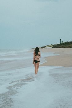 A woman in a bikini walks along the serene shoreline, enjoying a peaceful summer day.