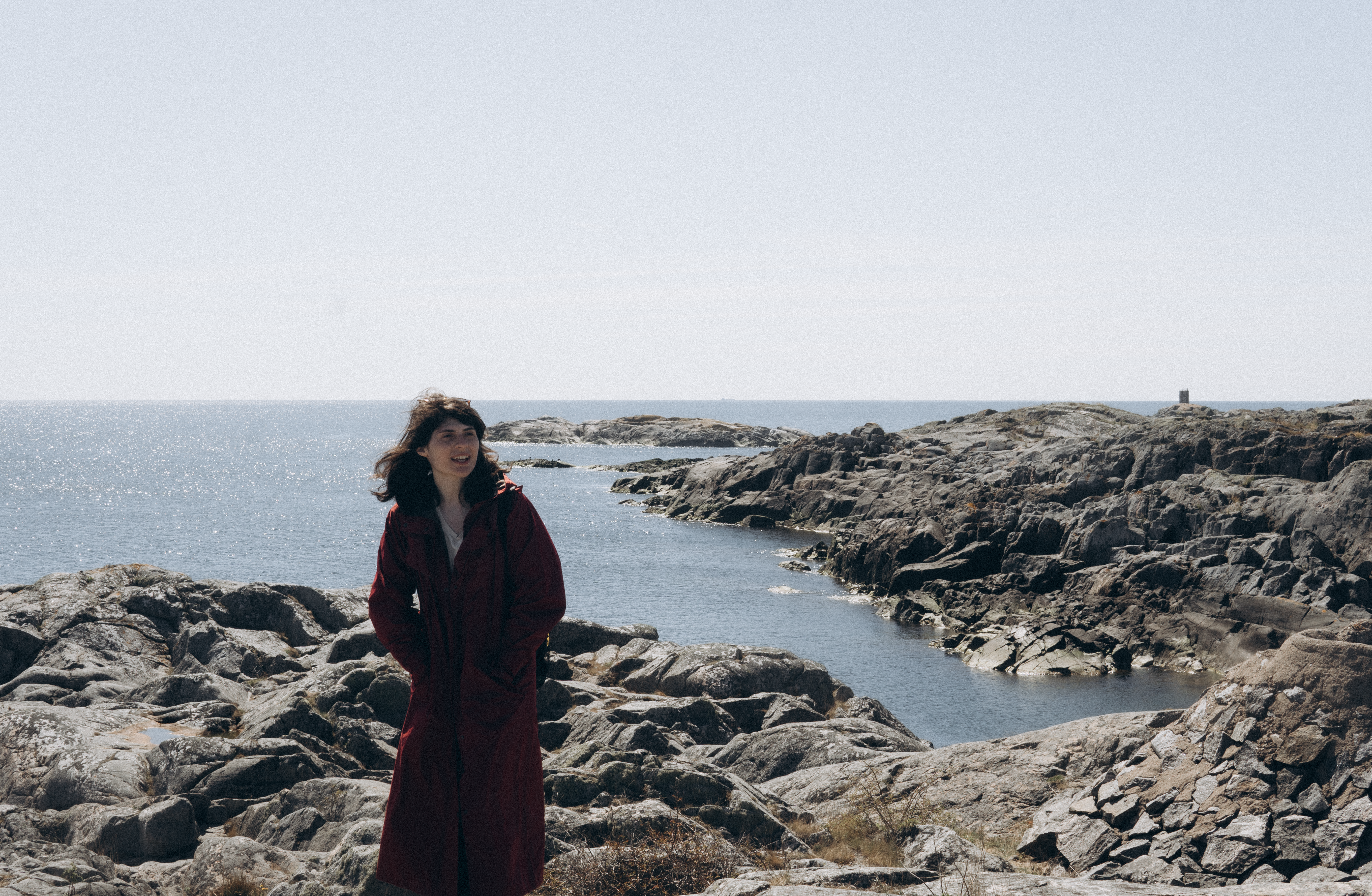 Woman in a Long Coat Standing on a Rocky Seashore · Free Stock Photo
