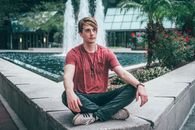 Man in Red and Blue Striped Crew Neck T-shirt and Black Pants Sitting on Concrete
