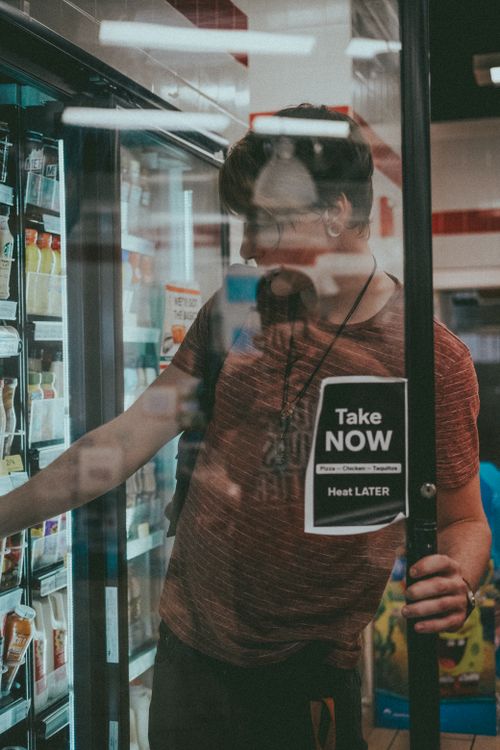 Free A young man selects groceries from a refrigerator in a supermarket aisle. Stock Photo