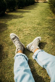 Teen wearing grey sneakers and blue jeans relaxing on grass outdoors.