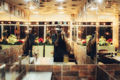 Person in a Green Shirt Taking a Picture in Front of a Wall Mirror