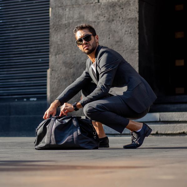 Man crouching on a street beside a large holdall — photo by Kuiyibo Campos on Pexels