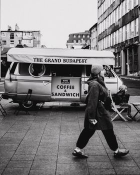A black and white photo of a coffee van with a walking woman in an urban setting.