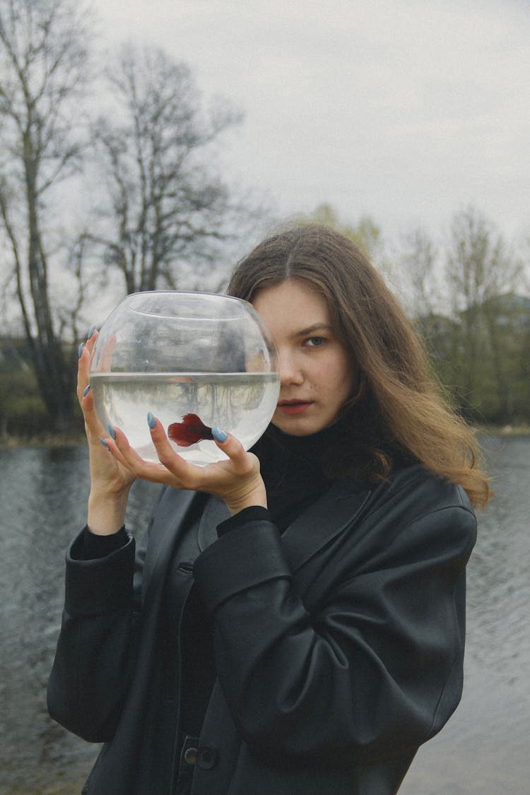 A Woman In Black Jacket Holding A Fish Bowl