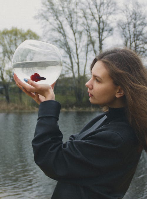 A Woman in Black Jacket Holding a Glass Fish Bowl
